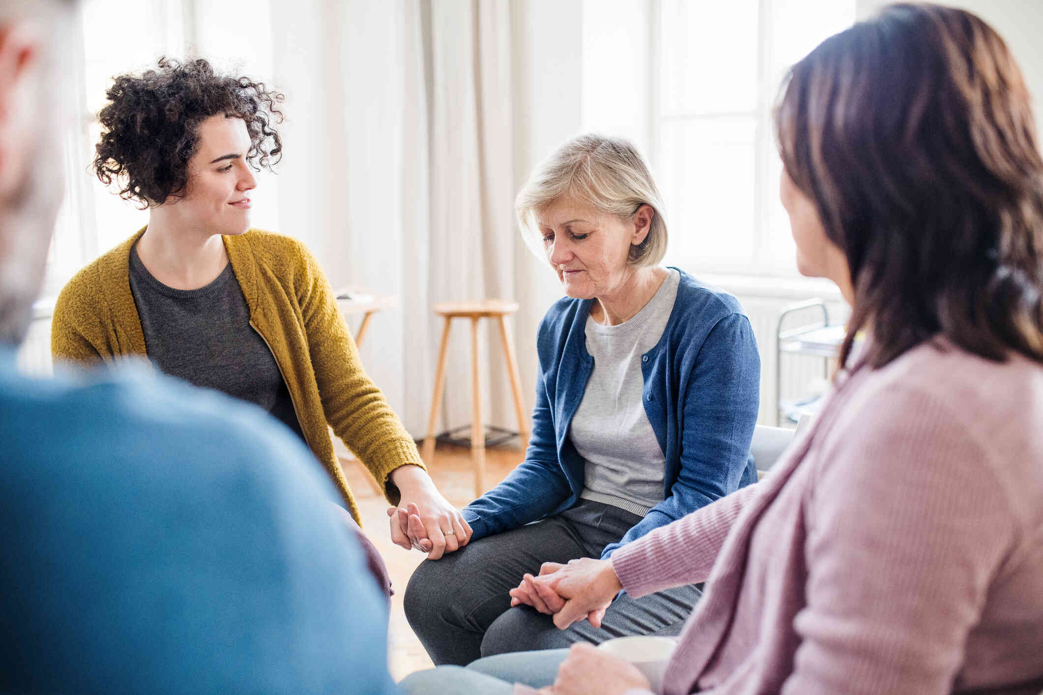 A group of women seated in a circle on chairs appears to be participating in a supportive group therapy session.